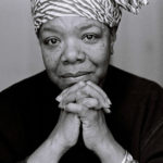 Maya Angelou in a dark shirt with her chin in her hands, smiling.