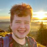 Jack, smiling, with a sparkling sun and trees taken from a mountaintop in the background.