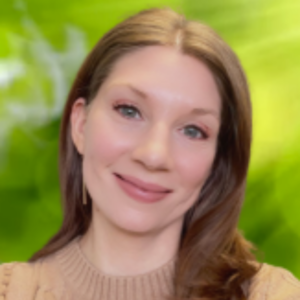 In a background of blurry green, Gina's wearing a brown sweater. She has long red hair and light skin.