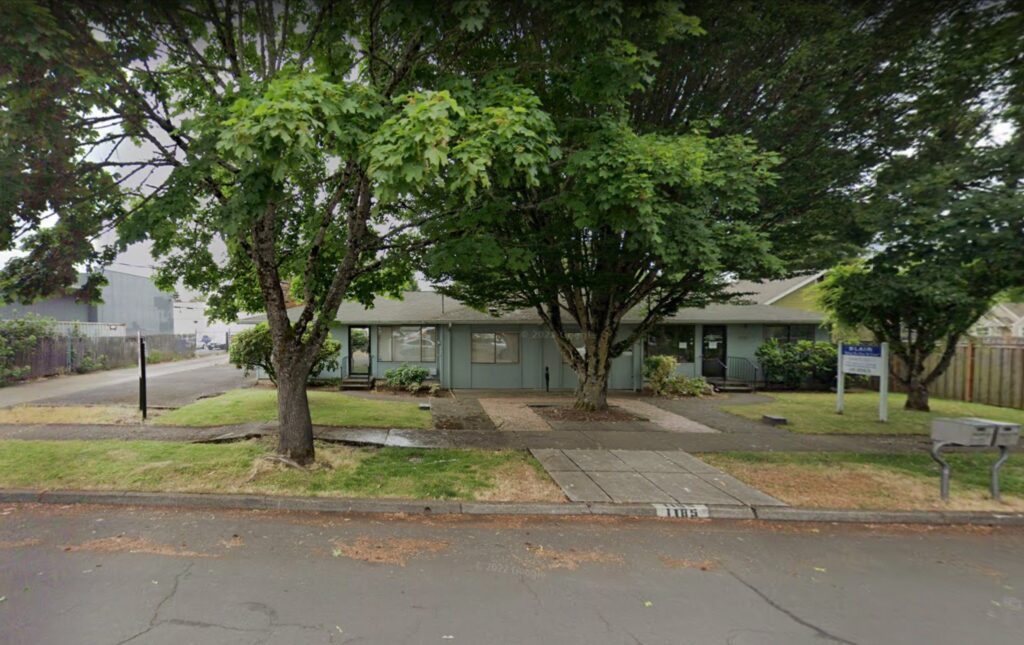 a blue-green one-story house with a couple trees in the front yard.