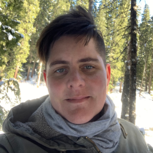 Danielle, wearing a earth-toned hoodie. Trees are in the background